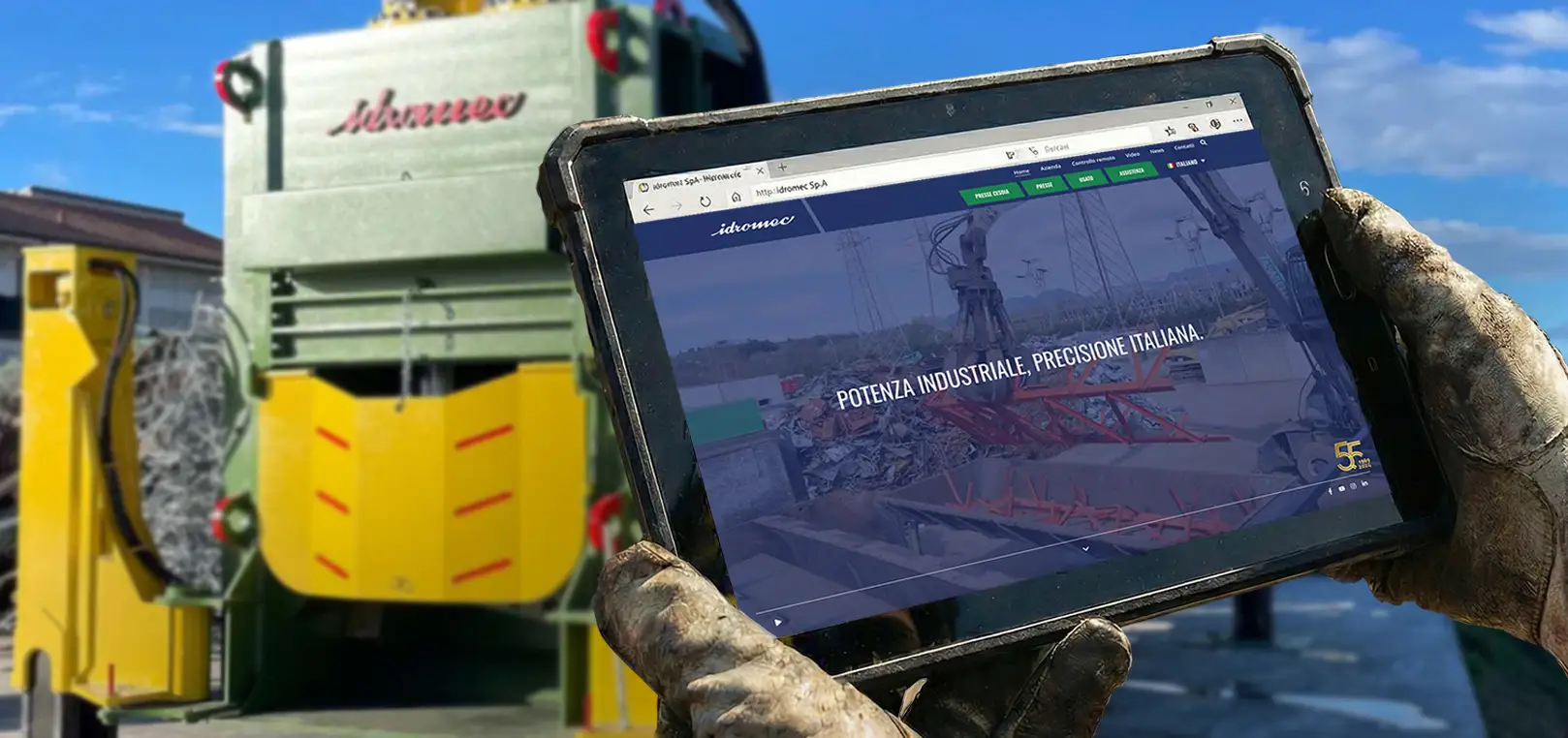 Nuovo sito Idromec visualizzato su tablet davanti a una pressa per rottami metallici